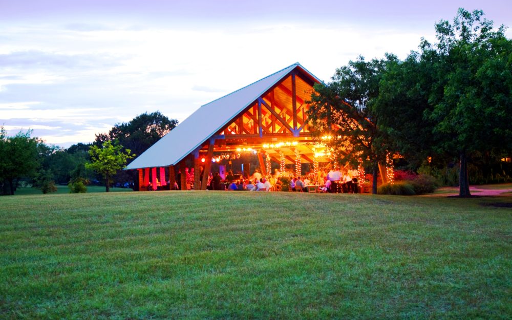 A wooden pavilion decorated for weddings on a green lawn in Texas.